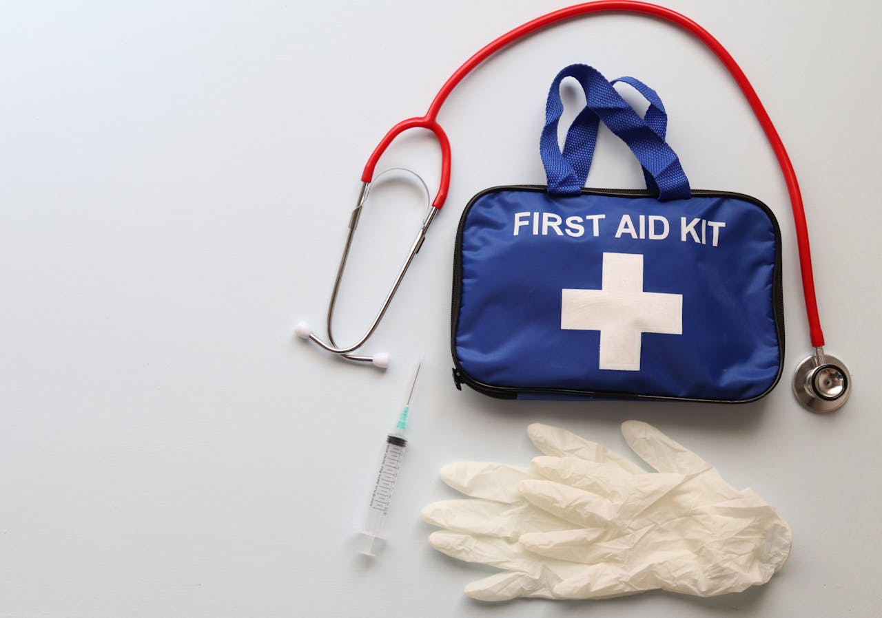 services-03 Flat lay of first aid kit, stethoscope, syringe, and gloves on white background.